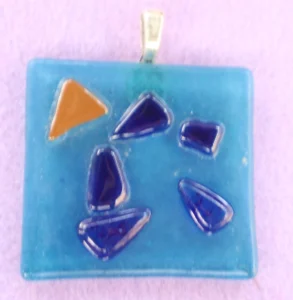 Pendentif grand carré bleu parsemé de 5 éclats bleu et un marron. Une bélière collée à l'arrière.