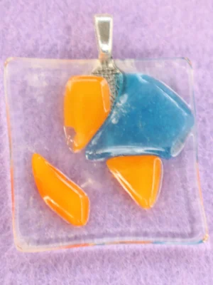 Pendentif en verre transparent avec un éclat bleu et 3 oranges, fondus à la surface. Une bélière collée à l'arrière