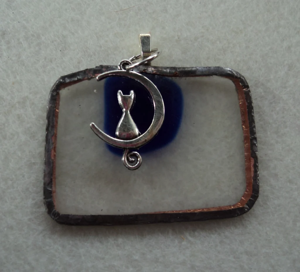 Pendentif en verre rectangulaire transparent avec un éclat bleu fondu. Monté en Tiffany. une breloque chat assis sur un croissant de lune.