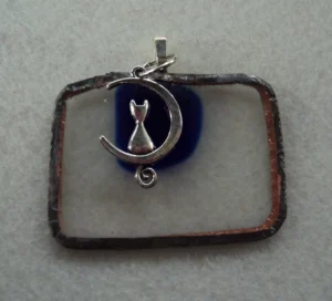 Pendentif en verre rectangulaire transparent avec un éclat bleu fondu. Monté en Tiffany. une breloque chat assis sur un croissant de lune.