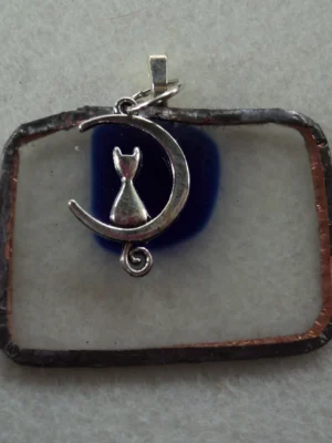 Pendentif en verre rectangulaire transparent avec un éclat bleu fondu. Monté en Tiffany. une breloque chat assis sur un croissant de lune.