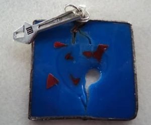 Pendentif carré bleu avec des éclats rouges, des fissures et une breloque clef à molette