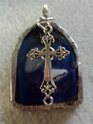 Pendentif en forme de baie d'église bleu avec des éclats gris et blancs. Un éclat blanc et un gris ont été fondus entre deux couches de verre, une transparente et une bleu nuit. Monté en Tiffany, une breloque en forme de croix a été accrochée à la bélière soudée à l'arrière.