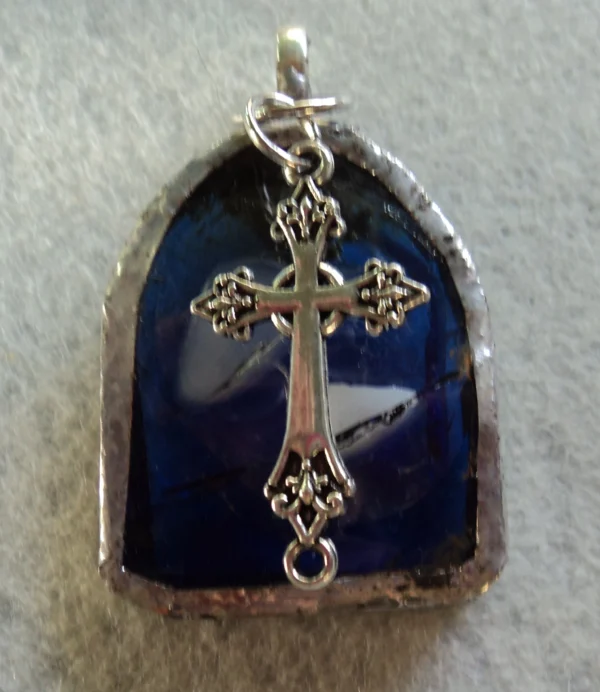 Pendentif en forme de baie d'église bleu avec des éclats gris et blancs. Un éclat blanc et un gris ont été fondus entre deux couches de verre, une transparente et une bleu nuit. Monté en Tiffany, une breloque en forme de croix a été accrochée à la bélière soudée à l'arrière.