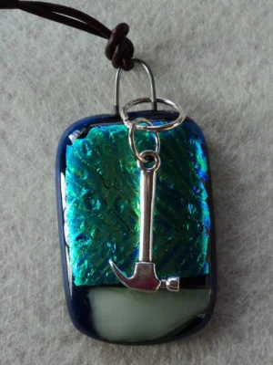 Pendentif en verre dichroïque bleu turquoise avec un tiret blanc au dessous, fondus sur du verre bleu nuit. Un anneau fondu entre 2 couches de verre a permis de fixer une breloque en forme de pioche