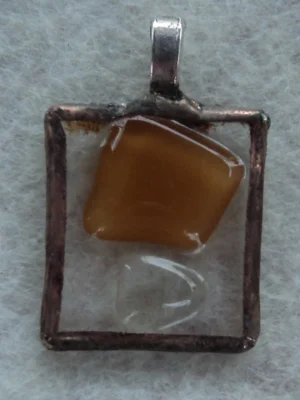 Pendentif rectangulaire en verre transparent avec un important éclat beige foncé souligné d'un petit transparent. Monté en Tiffany, une bélière est soudée à l'arrière.