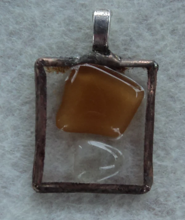 Pendentif rectangulaire en verre transparent avec un important éclat beige foncé souligné d'un petit transparent. Monté en Tiffany, une bélière est soudée à l'arrière.