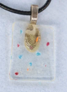 Pendentif en verre transparent avec une myriade d'éclats de verre multicolores fondus. Une bélière argentée collée à l'arrière