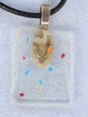 Pendentif en verre transparent avec une myriade d'éclats de verre multicolores fondus. Une bélière argentée collée à l'arrière