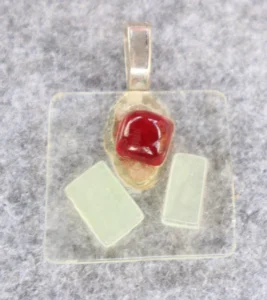 Pendentif en verre transparent avec 1 éclat rouge et 2 blancs. Une bélière collée.