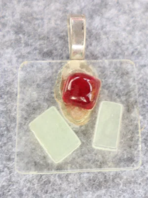 Pendentif en verre transparent avec 1 éclat rouge et 2 blancs. Une bélière collée.