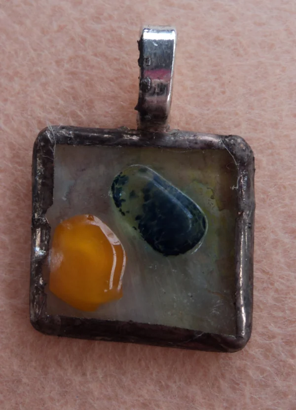 Petit pendentif carré en verre fondu avec des éclats orange et bleu. Monté en Tiffany, une bélière argentée.