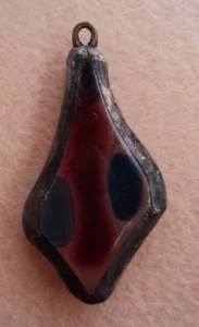 Pendentif en forme de losange irrégulier, en verre transparent, avec une lame rouge encadrée de 2 éclats bleus fondus à la surface, monté en Tiffany