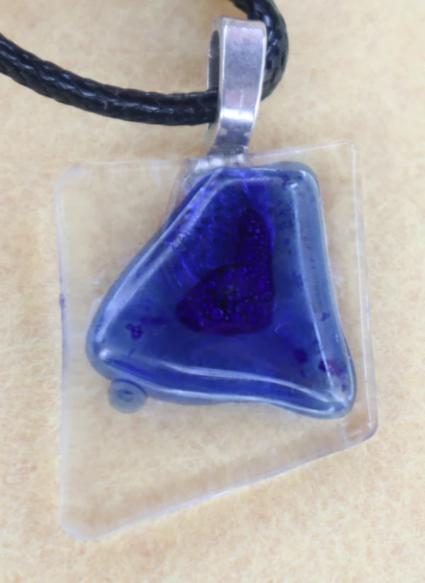 Pendentif en verre transparent avec un important éclat bleu fondu à la surface. Une bélière collée à l'arrière.