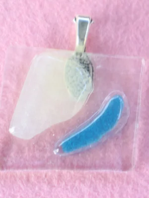 Pendentif en verre transparent sur lequel un éclat blanc et un bleu sont fondus. Une bélière en métal argentée est collée à l'arrière