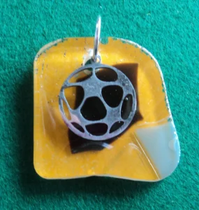 Pendentif en verre orange, avec des éclats noir et gris fondus. Une breloque en ballon de foot est suspendue à un anneau