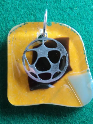 Pendentif en verre orange, avec des éclats noir et gris fondus. Une breloque en ballon de foot est suspendue à un anneau