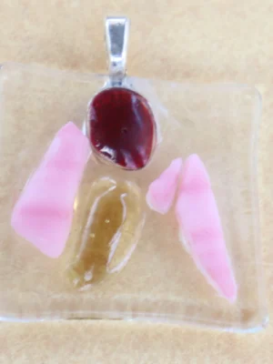 Pendentif carré en verre transparent, avec 5 éclats rose, orange et rouge, dépassant de la surface. Une bélière argentée collée à l'arrière.