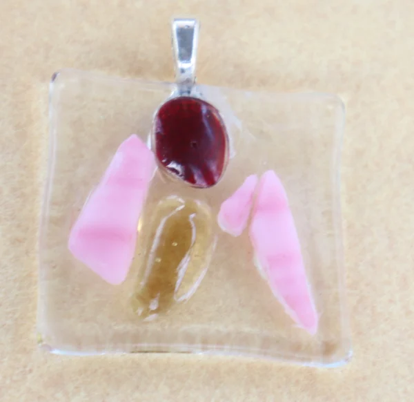 Pendentif carré en verre transparent, avec 5 éclats rose, orange et rouge, dépassant de la surface. Une bélière argentée collée à l'arrière.