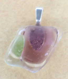 Pendentif en verre bleu avec des éclats rose et vert pastels. Une bélière collée à l'arrière.