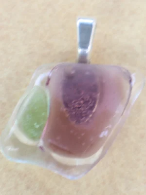 Pendentif en verre bleu avec des éclats rose et vert pastels. Une bélière collée à l'arrière.