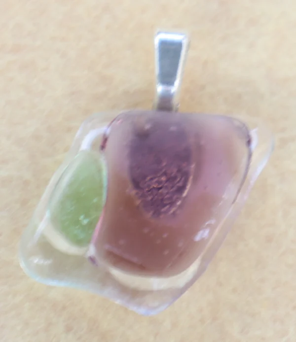 Pendentif en verre bleu avec des éclats rose et vert pastels. Une bélière collée à l'arrière.