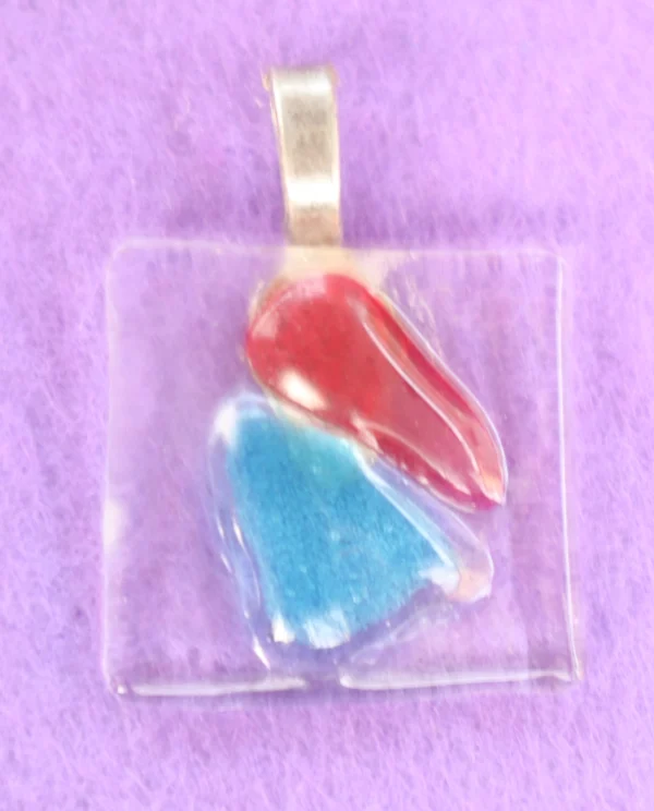 Pendentif rectangulaire en verre transparent avec deux éclats triangulaires bleu et rouge. Une bélière argentée est collée à l'arrière