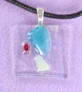 Pendentif rectangulaire en verre transparent, avec un éclat bleu, un blanc et un rouge plus petits. Une bélière en métal argenté est collée à l'arrière