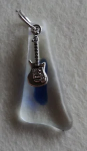 Pendentif triangulaire en verre transparent fondu avec une larme bleue. Un anneau argenté passé dans un orifice au sommet a permis de suspendre une breloque en forme de guitare