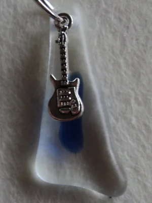 Pendentif triangulaire en verre transparent fondu avec une larme bleue. Un anneau argenté passé dans un orifice au sommet a permis de suspendre une breloque en forme de guitare