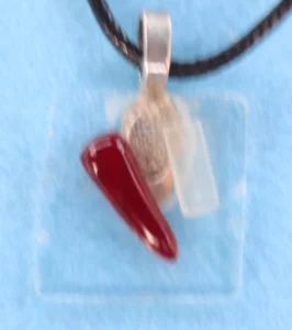 Petit pendentif en verre fin avec un éclat blanc et un rouge. Une bélière argentée collée à l'arrière.