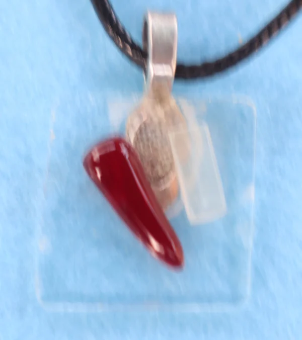 Petit pendentif en verre fin avec un éclat blanc et un rouge. Une bélière argentée collée à l'arrière.