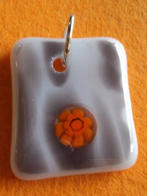 Pendentif en verre blanc strié de gris avec un millefiori orange fondu à sa surface et un anneau argenté pour la fixation