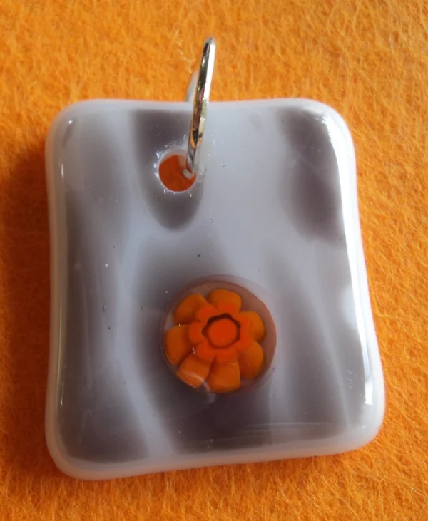 Pendentif en verre blanc strié de gris avec un millefiori orange fondu à sa surface et un anneau argenté pour la fixation