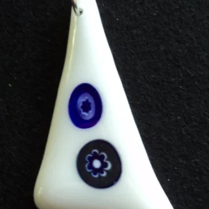 Pendentif triangulaire en verre blanc avec 2 millefioris bleus et blancs étirés par la fusion. Un anneau argenté passé dans un orifice au sommet