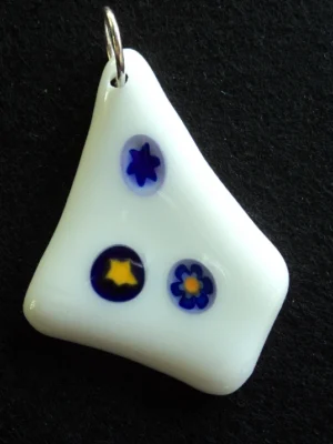 Pendentif en verre blanc en forme de losange irrégulier, avec 3 millefioris bleus, deux avec un cœur jaune. Un anneau argenté permet de le suspendre à une chaîne ou un lacet