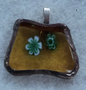 Pendentif fusing composé de 2 millefioris verts et blancs fondus sur un trapèze de verre orange transparent, monté en Tiffany avec une bélière argenté soudée à l'arrière