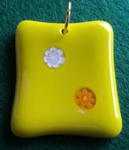 Pendentif en verre jaune avec un millefiori blanc et un orange. Un anneau doré pour la fixation