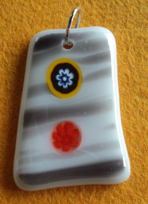 Pendentif en forme de trapèze en verre blanc strié de gris, 2 millefioris, un bleu et un orange, sont fondus à la surface