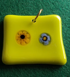 Pendentif rectangulaire en verre jaune sur lequel un milefiori range et un bleu pâle sont fondus, un orifice au sommet permet de passe un anneau doré