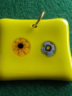 Pendentif rectangulaire en verre jaune sur lequel un milefiori range et un bleu pâle sont fondus, un orifice au sommet permet de passe un anneau doré