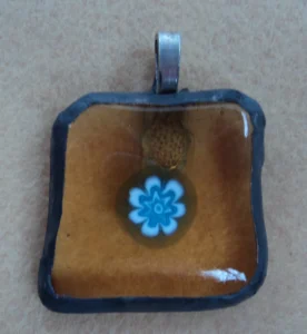 Pendentif composé d'un millefiori bleu et blanc sur verre orange transparent, monté selon la technique Tiffany