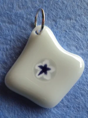 Pendentif en verre blanc, de forme irrégulière, avec un millefiori bleu cerné de blanc étiré par la fusion en forme de feuille étoilée