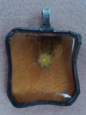 Pendentif avec un simple millefiori jaune sur fond orange transparent, monté en Tiffany