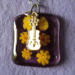 Pendentif en verre mauve  semi transparent avec 6 millefioris jaune fondus. Une breloque en métal doré en forme de guitare.