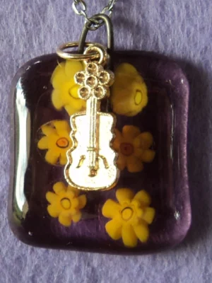 Pendentif en verre mauve semi transparent avec 6 millefioris jaune fondus. Une breloque en métal doré en forme de guitare.