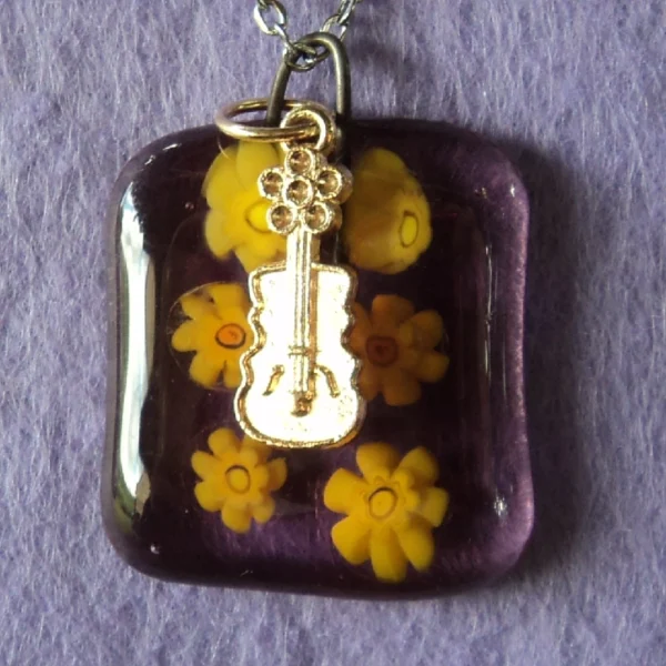 Pendentif en verre mauve semi transparent avec 6 millefioris jaune fondus. Une breloque en métal doré en forme de guitare.