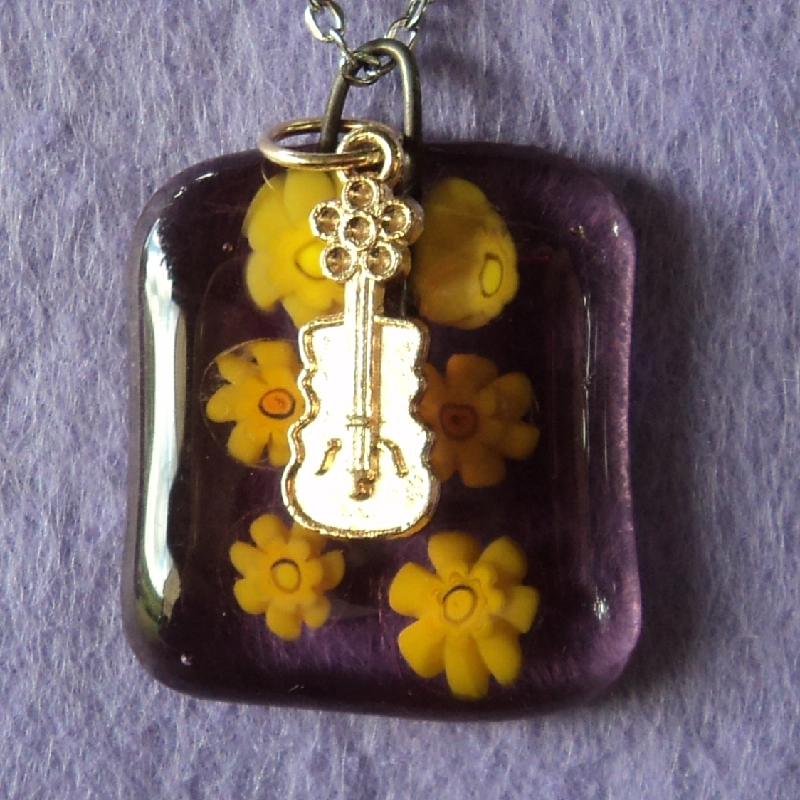 Pendentif en verre mauve semi transparent avec 6 millefioris jaune fondus. Une breloque en métal doré en forme de guitare.