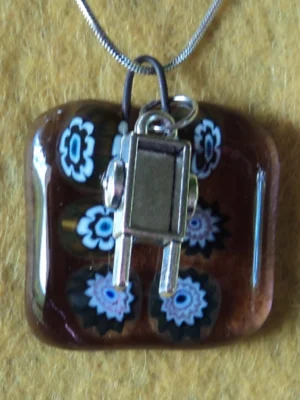 Pendentif en verre mauve semi transparent avec 6 millefioris blanc et noir et une breloque brouette.