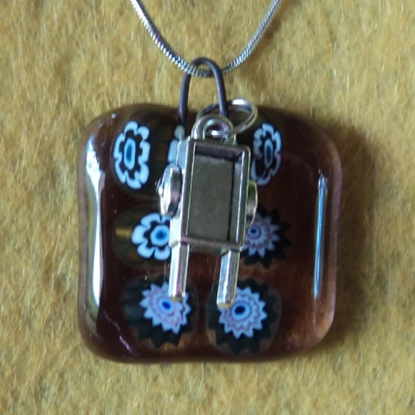 Pendentif en verre mauve semi transparent avec 6 millefioris blanc et noir et une breloque brouette.